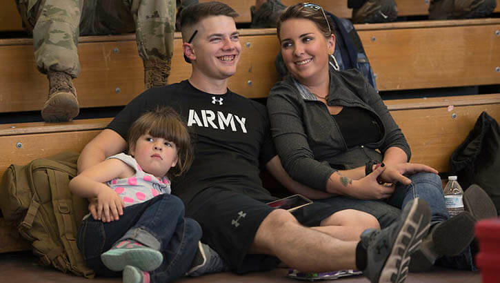 Image of Soldier sitting in gym with wife and daughter. Click to open a larger version of the image.