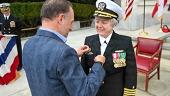 Capt. Darla Dietrich, commanding officer of Navy Medicine Readiness and Training Command (NMRTC) Bethesda, is adorned with the command pin by her husband during a combined change of command and retirement ceremony,