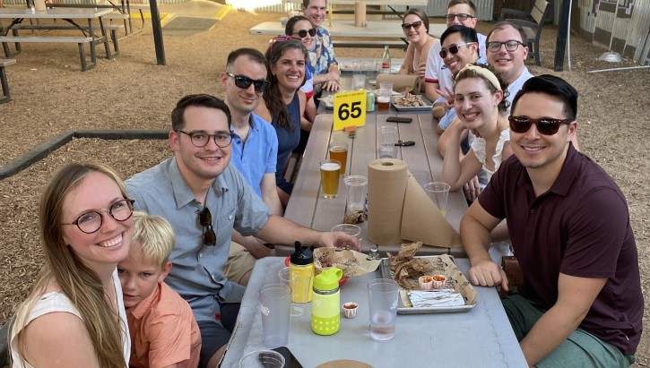 A group of people sitting a picnic table smiling at the camera.  
