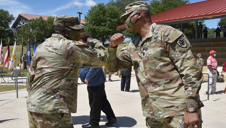 Two military personnel, wearing masks, giving each other an elbow bump