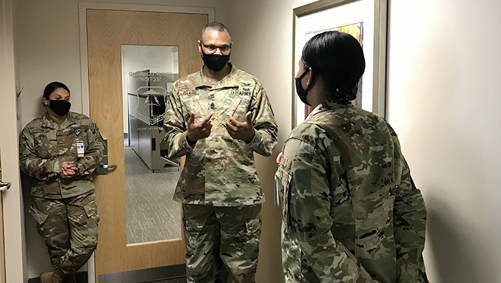 Three military personnel, wearing masks, having a discussion in a room