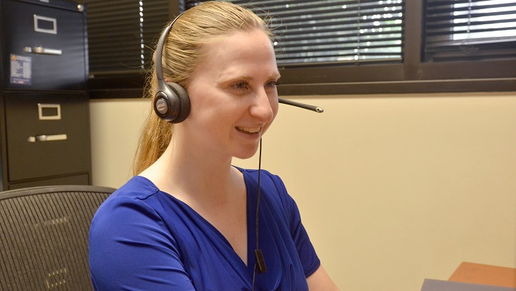Image of smiling woman with telephone headset sitting at her desk