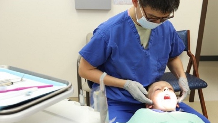 Image of Military health personnel wearing a face mask examines the mouth of a child. Click to open a larger version of the image.