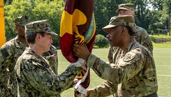 Uniformed Services University President Dr. Jonathan Woodson, a retired Army major general, passes the University's colors to Navy Capt. Tammy Servies