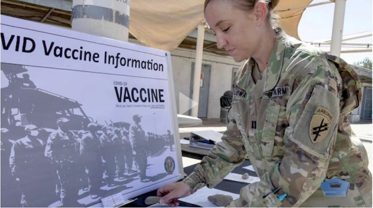 Image of soldier looking through COVID vaccine information laid out on a table